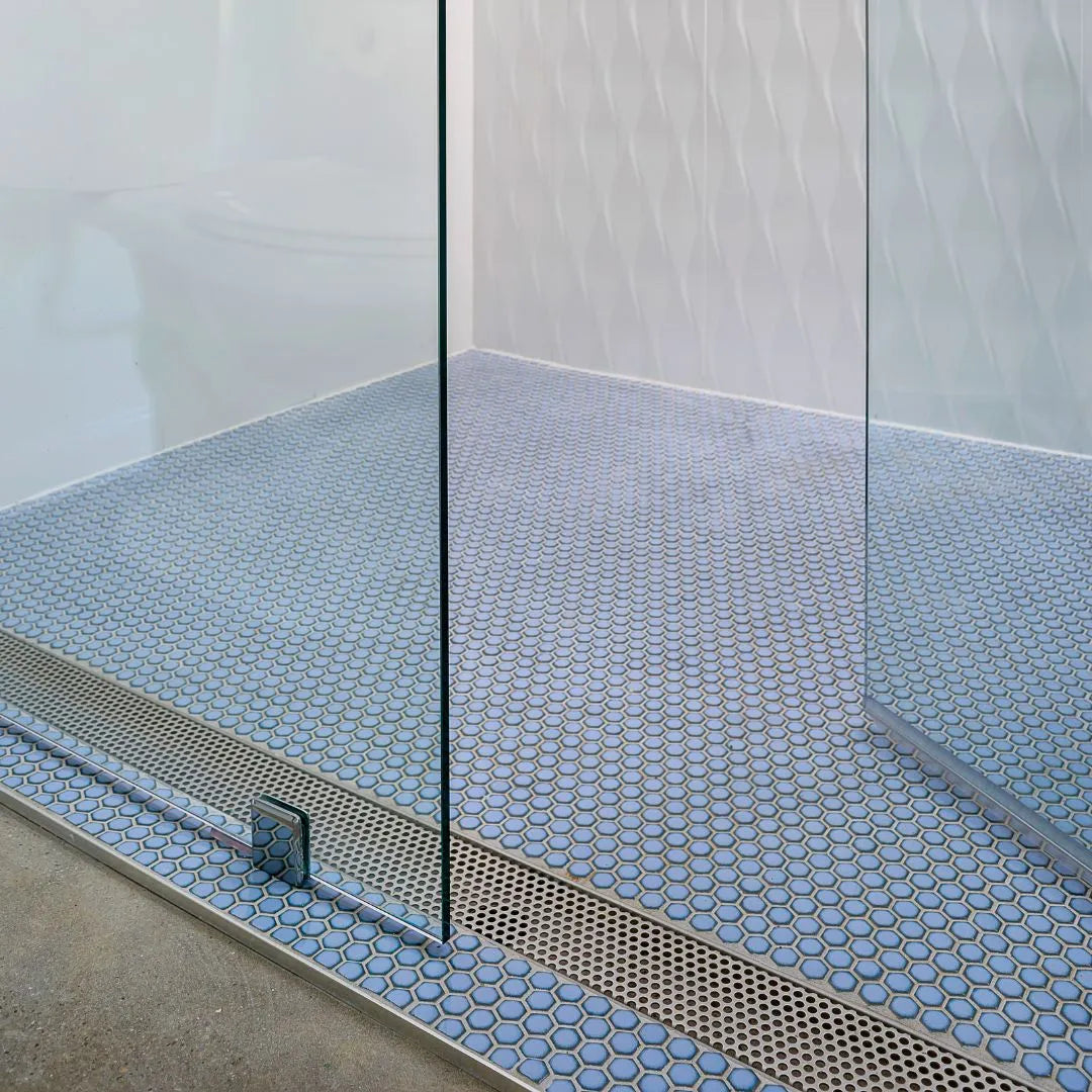 Modern commercial space featuring white oak wood flooring with a Perforated Adjustable Delmar Linear Drain seamlessly integrated along a floor joint—stainless-steel channel with precision perforated grate, adjustable frame, and integrated flange for efficient high-capacity drainage.
