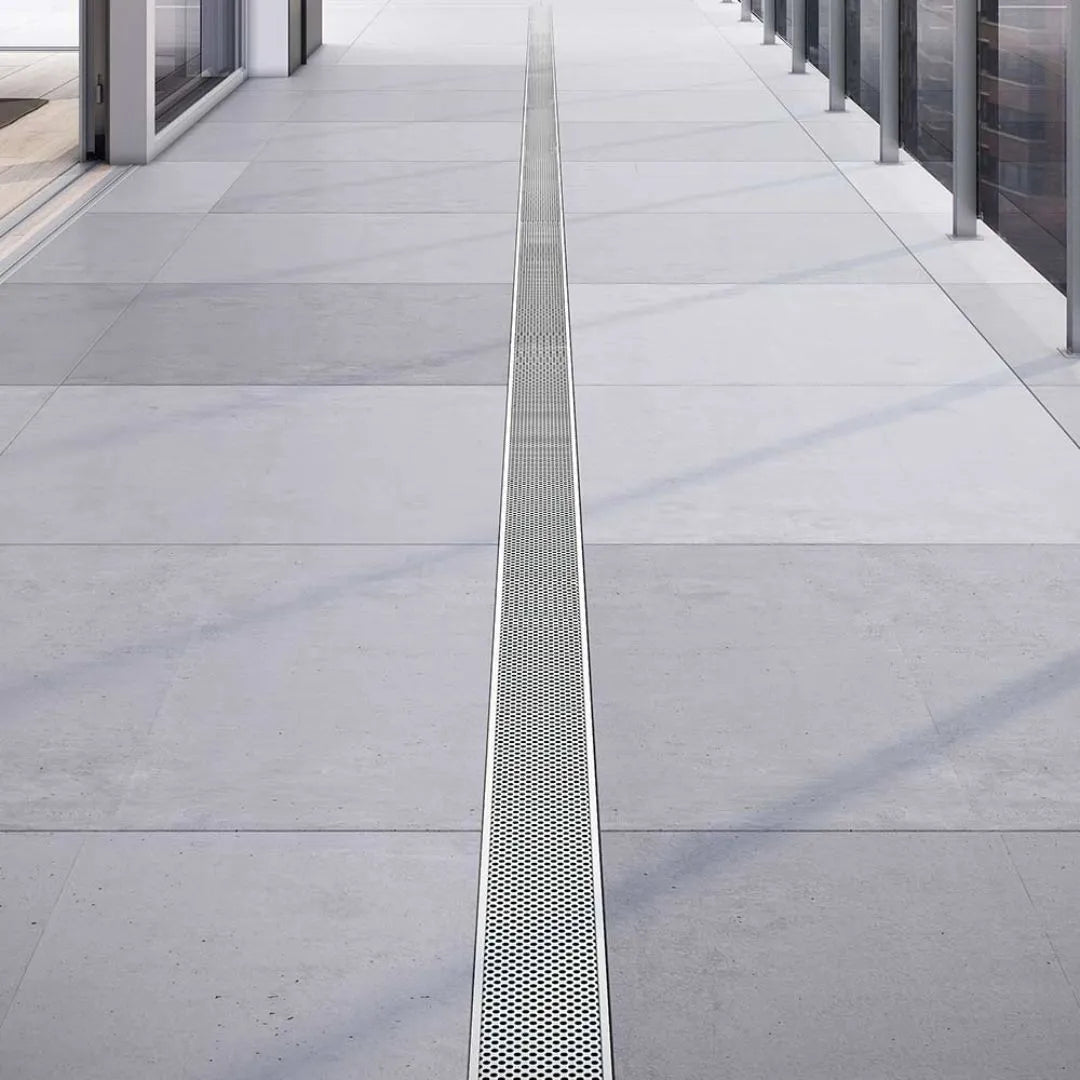 Modern outdoor setting showcasing the Perforated Outdoor Linear Drain—heavy-duty stainless-steel channel with precision perforated grate, integrated flange beneath stone pavers, and high-capacity drainage for efficient water management in exterior landscapes.
