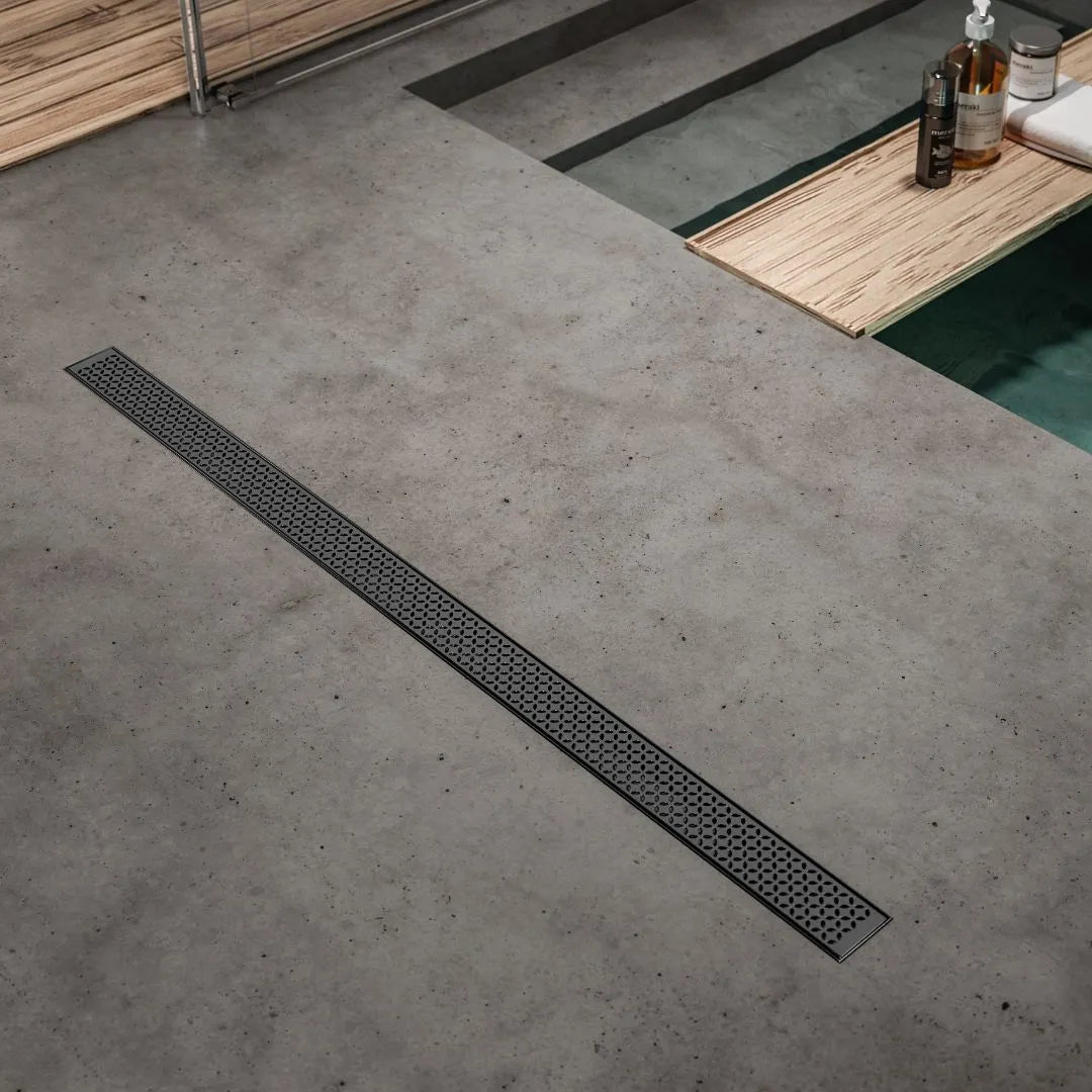 QM Drain Lotus Walking Shower in Black finish, featuring a sleek stainless-steel linear drain integrated into the shower floor. The drain offers efficient water drainage, a minimalist design with a perforated grate, and a modern aesthetic for contemporary luxury shower installations.