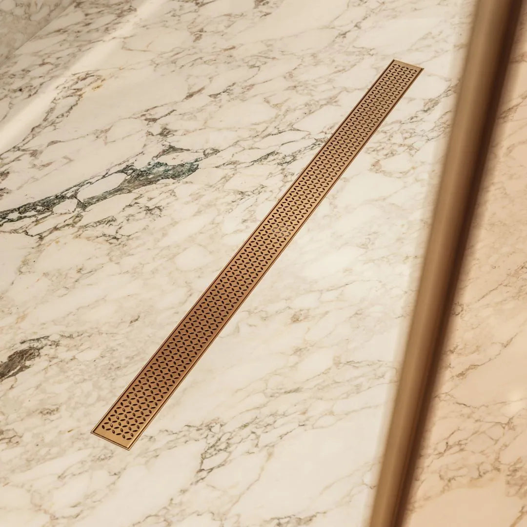 QM Drain Lotus Linear Drain in Bronze, featuring a sleek stainless-steel channel with a modern perforated grate design. This drain offers efficient water drainage and seamless integration into high-end shower floors, enhancing the minimalist and luxurious aesthetic of contemporary bathroom designs.