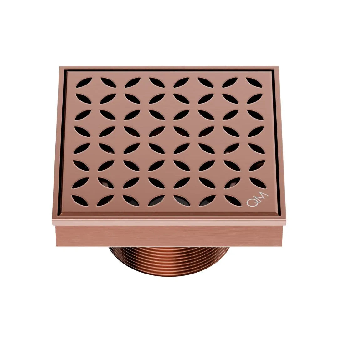 QM Drain Delmar Lotus Square Drain 4x4-inch in Bronze finish, featuring a sleek stainless-steel channel with an elegant floral-pattern grate. This drain offers efficient water drainage, seamless tile integration, and an elegant aesthetic, ideal for luxury shower and bathroom floor installations.