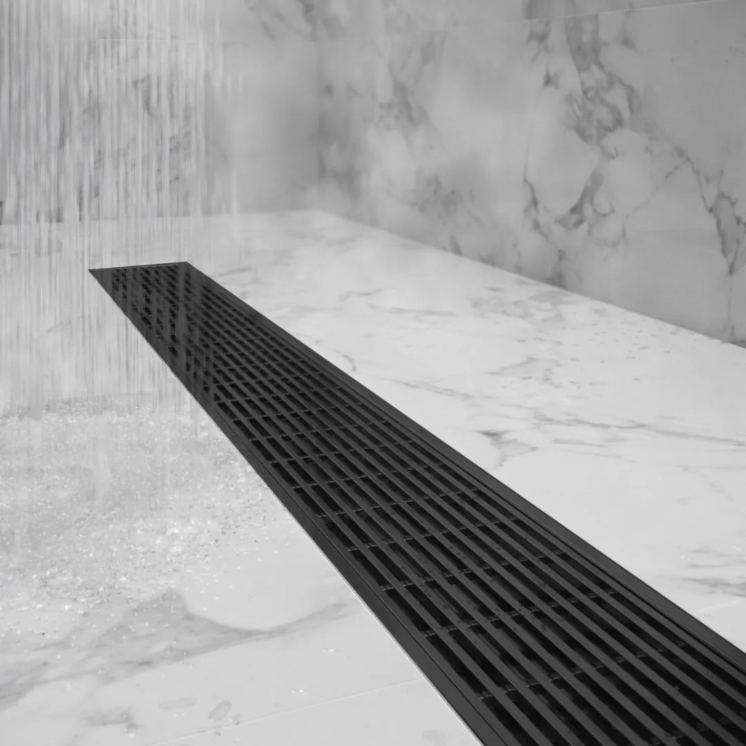 Top-down shot of bathroom floor featuring Delmar flange-edge drain in polished finish, emphasizing the flush grate, perimeter flange, and high-flow wedge-wire design.