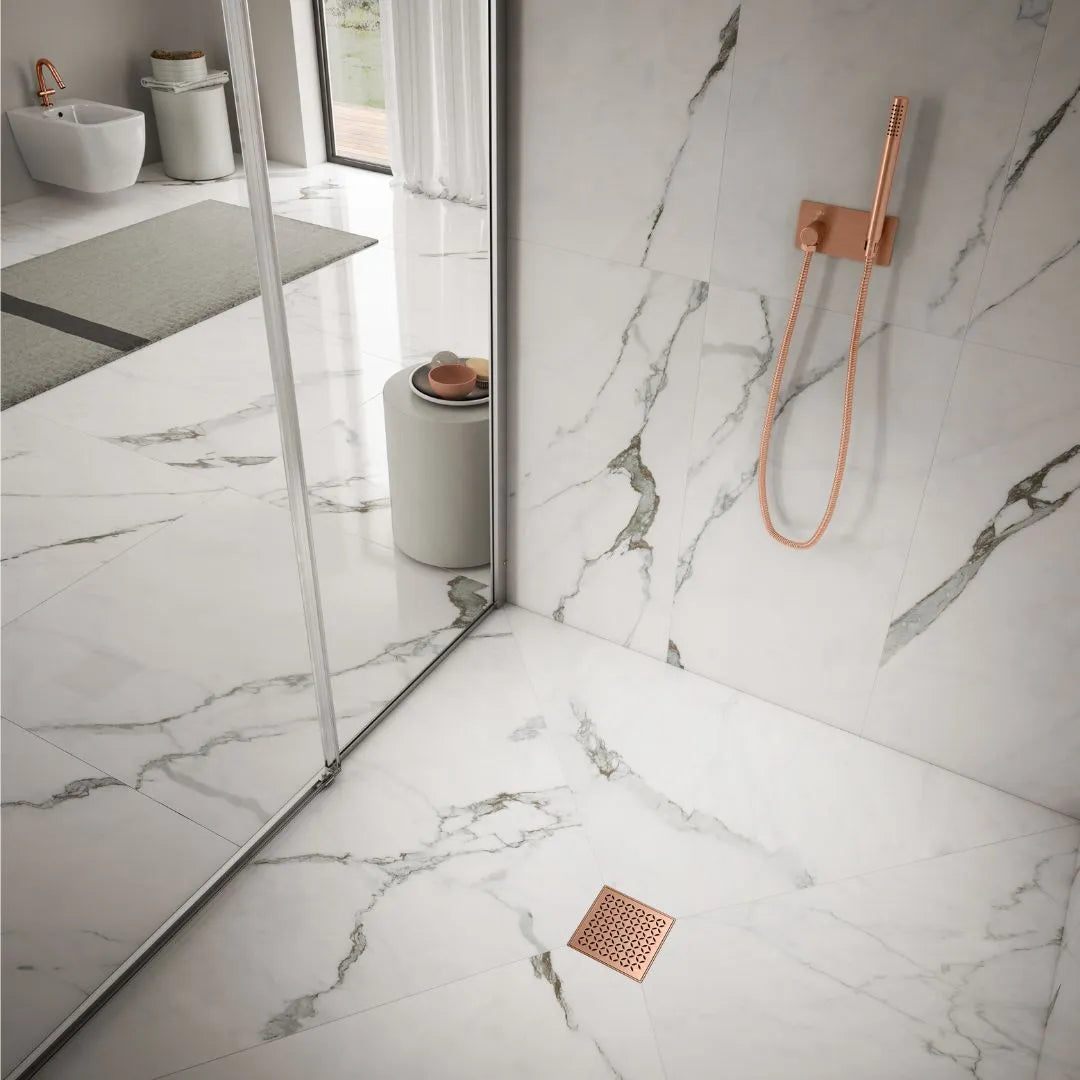 QM Drain Delmar Lotus Square Drain installed in modern showers, available in 4-inch and 5 3/4-inch sizes. Featuring a sleek stainless-steel floral-pattern grate, these drains offer efficient water drainage and seamless tile integration for luxury bathroom installations.