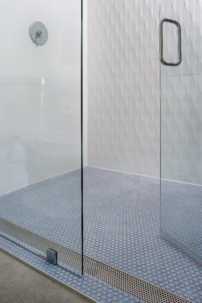 Perforated Adjustable Delmar Linear Drain in a commercial setting with white oak wood flooring. Stainless-steel channel with precision perforated grate, adjustable frame, and integrated flange for efficient, high-capacity drainage and seamless integration into the floor design.