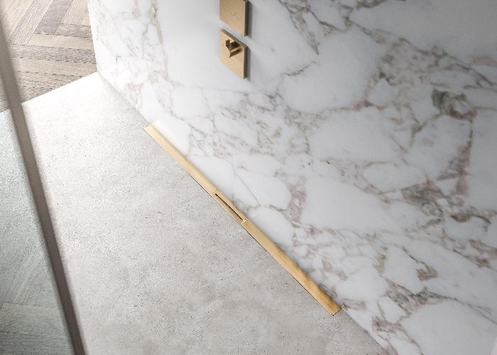 QM Drain Supreme Linear Drain in Gold finish, installed in a luxury bathroom setting. Featuring a sleek stainless-steel channel with a contemporary grate design, this drain offers seamless tile integration and efficient water drainage, enhancing the modern, elegant aesthetic of high-end shower and bathroom floor installations.