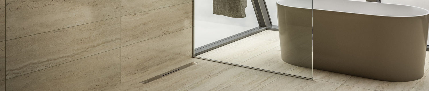 Hero banner showing a contemporary bathroom interior with a sleek linear shower drain from the QM Drain collection, showcasing the full range of premium drains and accessories.
