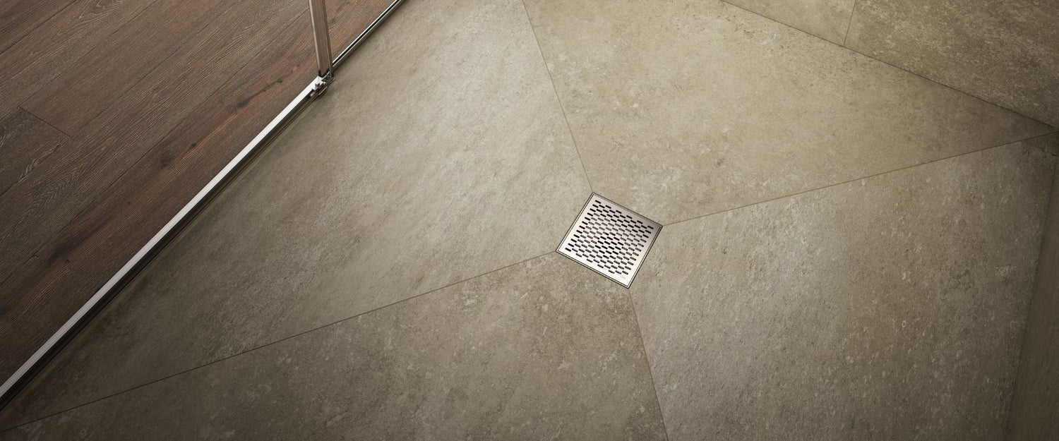 Banner showing a Delta Center Drain installed in a bathroom floor, highlighting premium stainless steel construction, modern design, and durable performance by QM Drain.