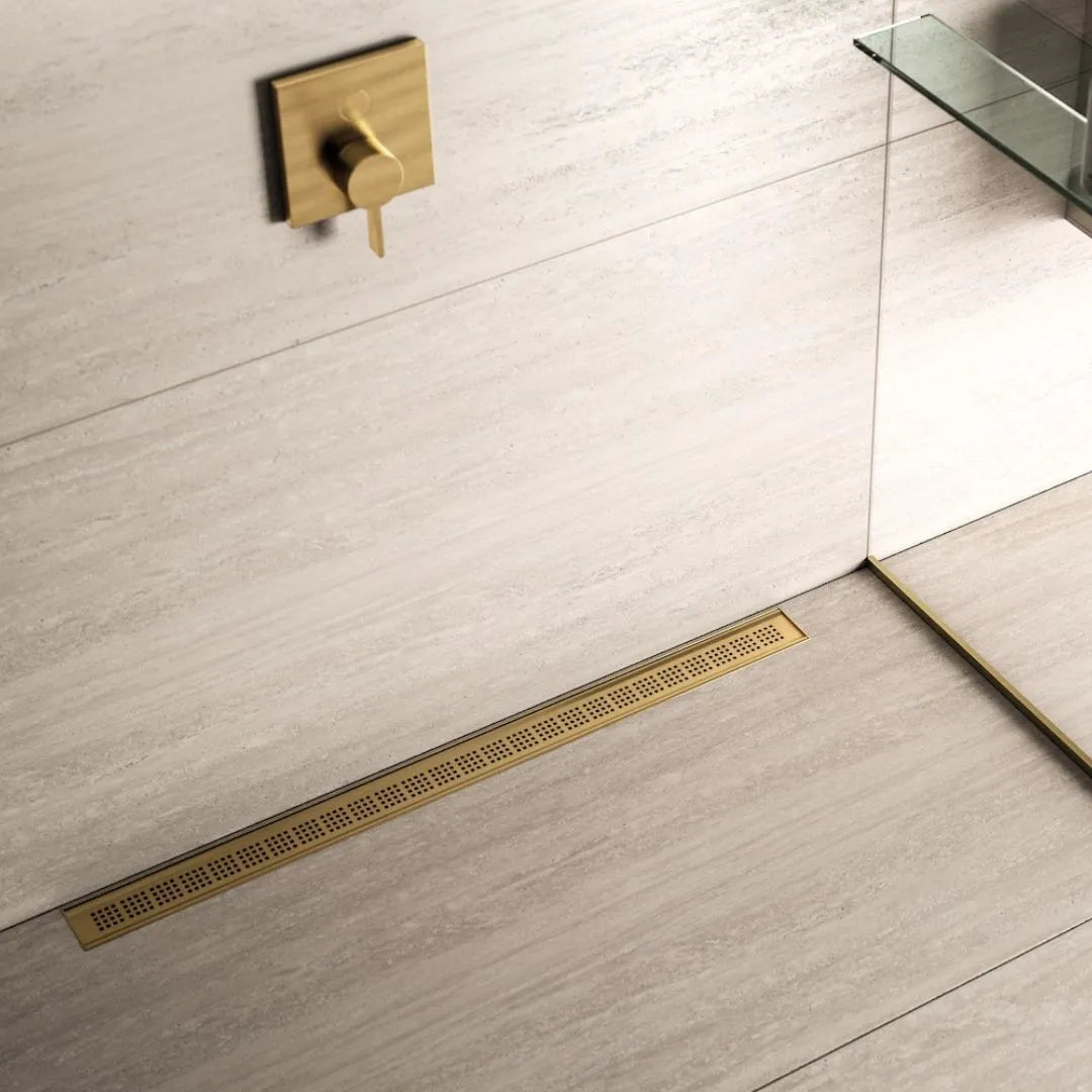 QM Drain Ria Linear Drain installed in Gold, Black, and Polished finishes, showcasing sleek stainless-steel channels with a modern perforated grate design. This drain provides efficient water drainage and seamless integration into luxury shower floors, offering a sophisticated, minimalist aesthetic.