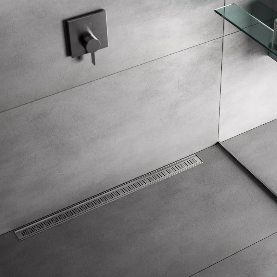 QM Drain Ria Linear Drain installed in Gold, Black, and Polished finishes, showcasing sleek stainless-steel channels with a modern perforated grate design. This drain provides efficient water drainage and seamless integration into luxury shower floors, offering a sophisticated, minimalist aesthetic.