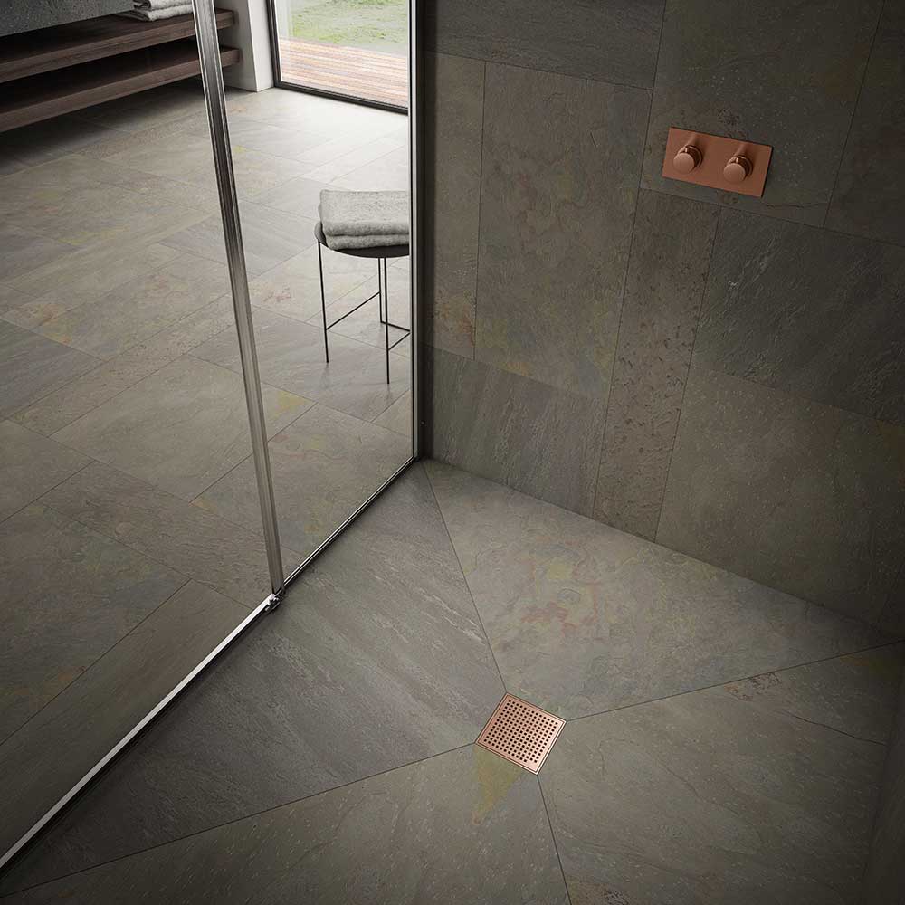 Modern shower floor showcasing the QM Drain Mira Square Drain in Bronze finish—4″×4″ stainless-steel tile-insert grate with subtle curved slots, integrated waterproof flange, and efficient high-flow drainage for sleek, contemporary bathroom designs.