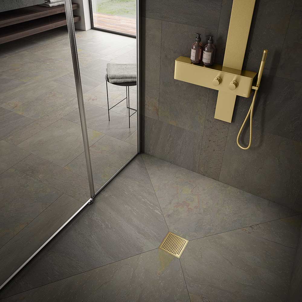 Modern shower floor showcasing the QM Drain Mira Square Drain in Gold finish—4″×4″ stainless-steel tile-insert grate with subtle curved slots, integrated waterproof flange, and efficient high-flow drainage for sleek, contemporary bathroom designs.